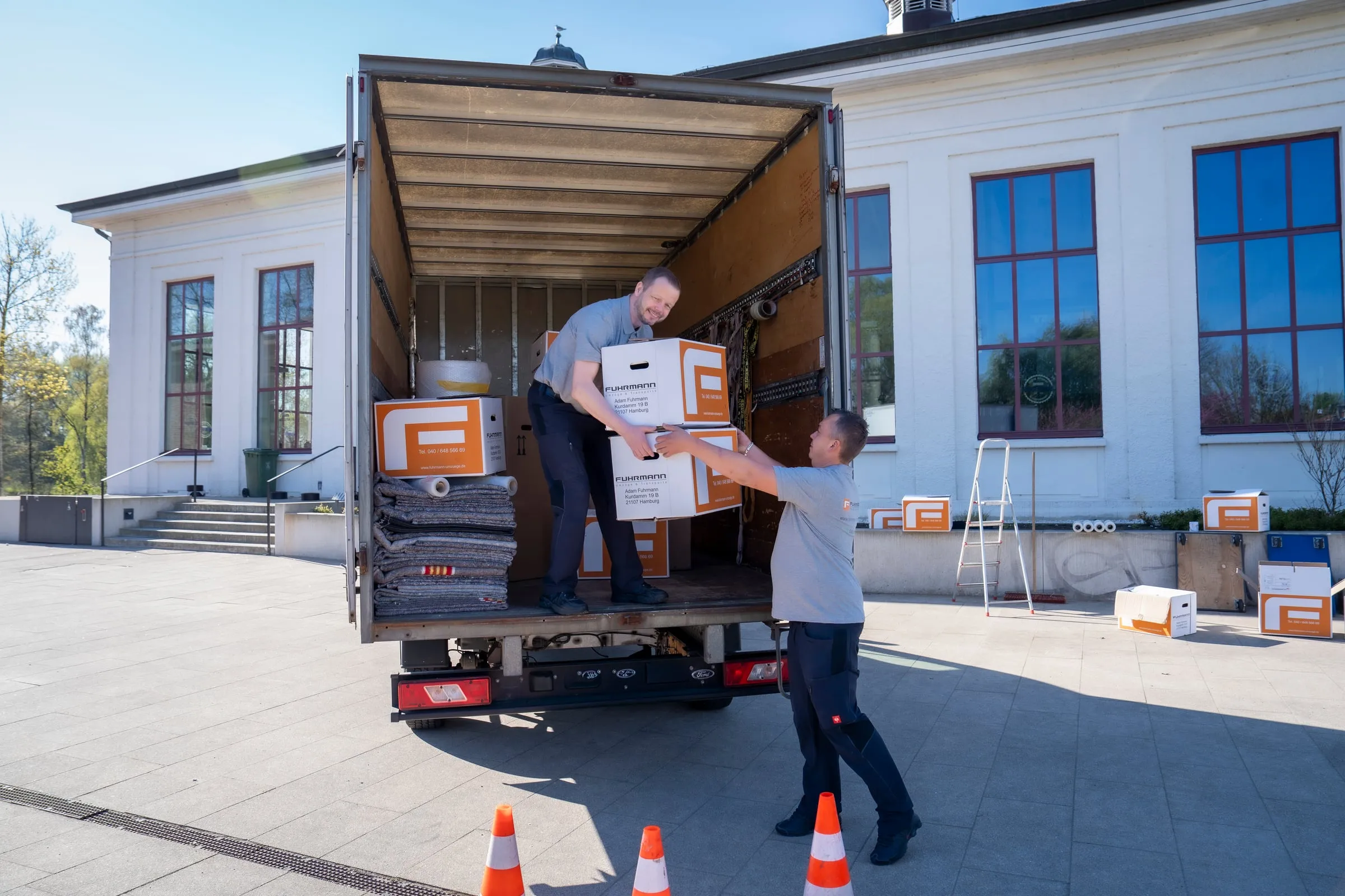 Zwei Fuhrmann-Mitarbeiter entladen Umzugskartons am LKW – Hamburger Umzugsteam in Aktion